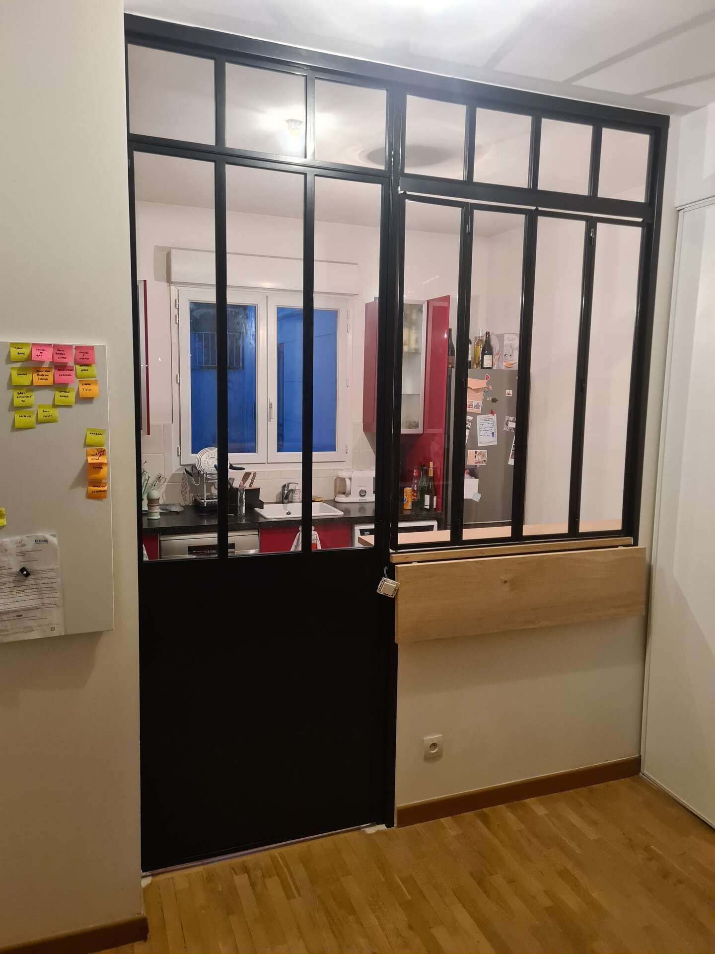 Une fenêtre intérieure avec des barreaux métalliques noirs, une porte noire et un comptoir.