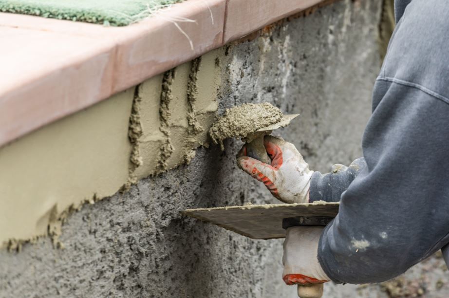 Un trabajador, con guantes puestos, aplica mortero a una pared de hormigón con una llana.