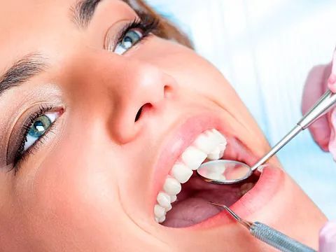Mujer en el dentista con la boca abierta, siendo examinada con un espejo y una sonda.