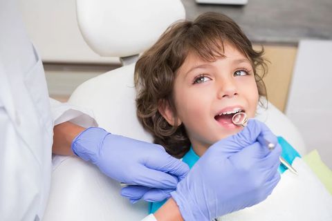 Niño en la silla del dentista, con la boca abierta para el examen; el dentista sostiene un espejo.