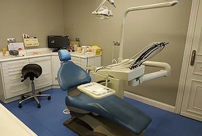 Consultorio dental con silla azul, equipamiento y un pequeño taburete negro.
