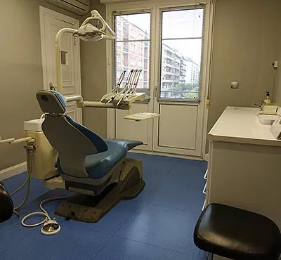 Operatorio dental con silla azul, herramientas, armarios blancos y ventana con vistas a la ciudad.