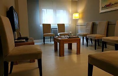 Sala de espera con sillas, mesa, ventana y lámpara encendida.