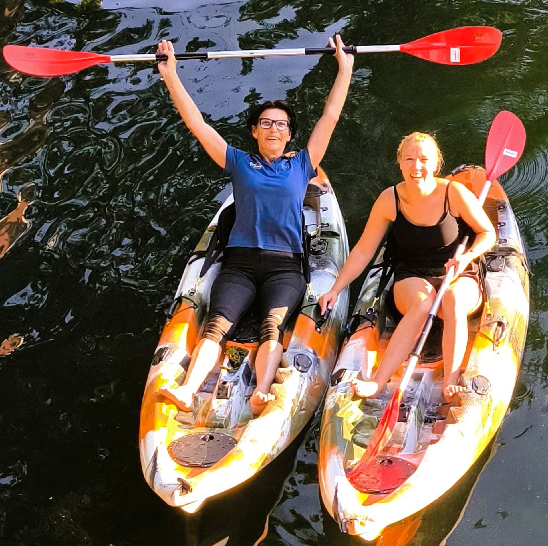 Zwei Frauen in Kajaks mit ihren Armen in der Luft
