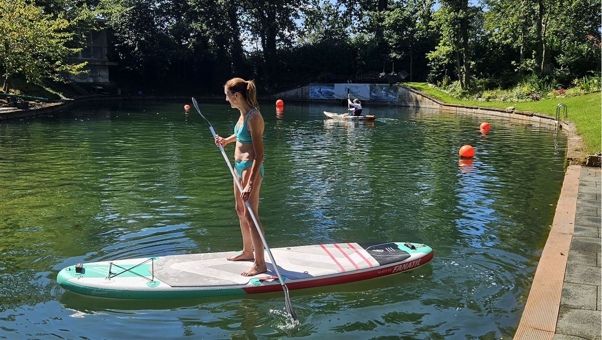 Eine Frau im Bikini steht auf einem Paddleboard im Wasser.