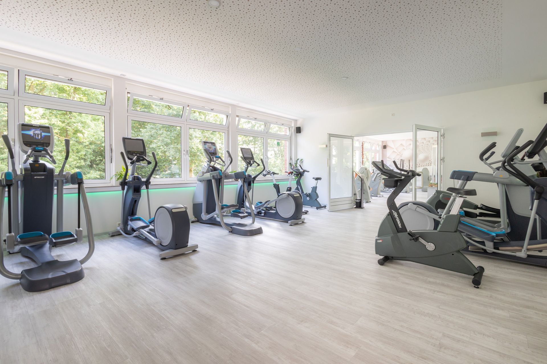 Ein Fitnessstudio mit vielen Trainingsgeräten und vielen Fenstern.