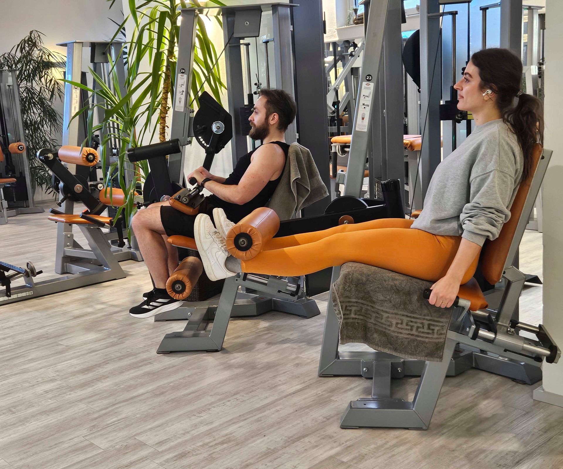 Ein Mann und eine Frau sitzen in einem Fitnessstudio auf Beinstreckergeräten.