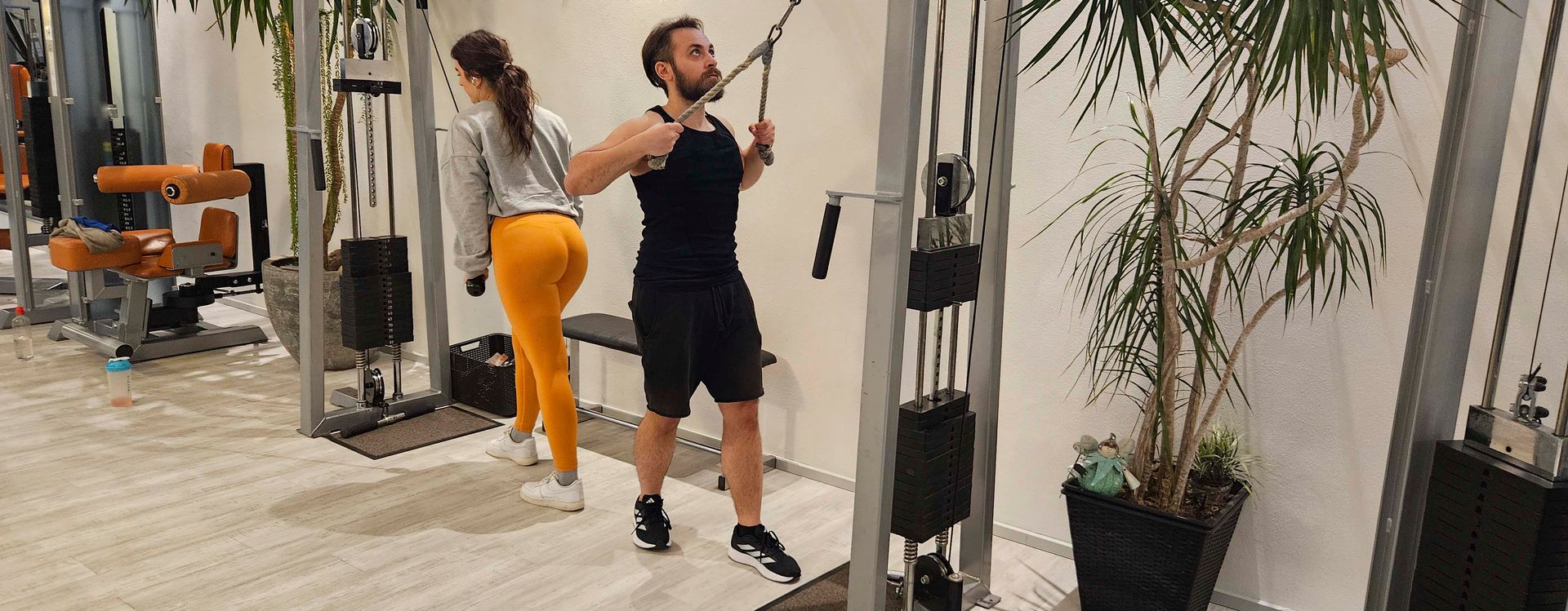 Ein Mann und eine Frau benutzen ein Gerät in einem Fitnessstudio.
