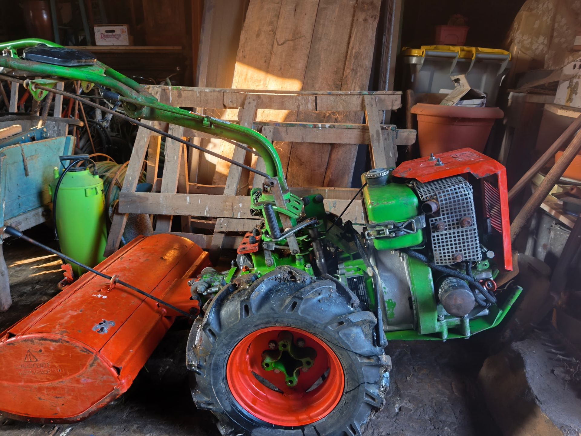 Tracteur vert avec accessoires orange garé dans un hangar encombré