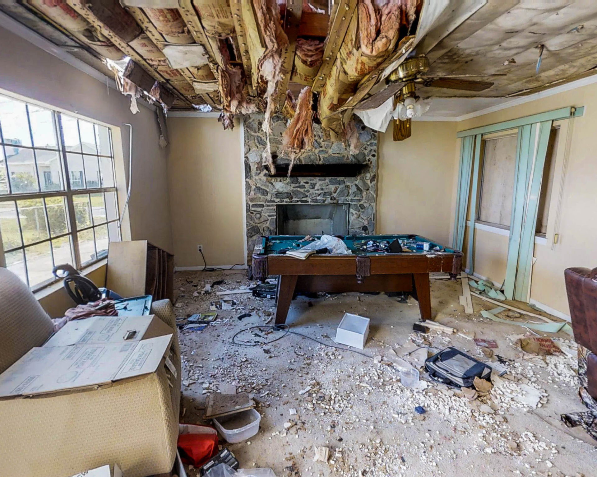 Intérieur d'une pièce endommagée : débris sur le sol, une table de billard, une cheminée en pierre et un plafond effondré.