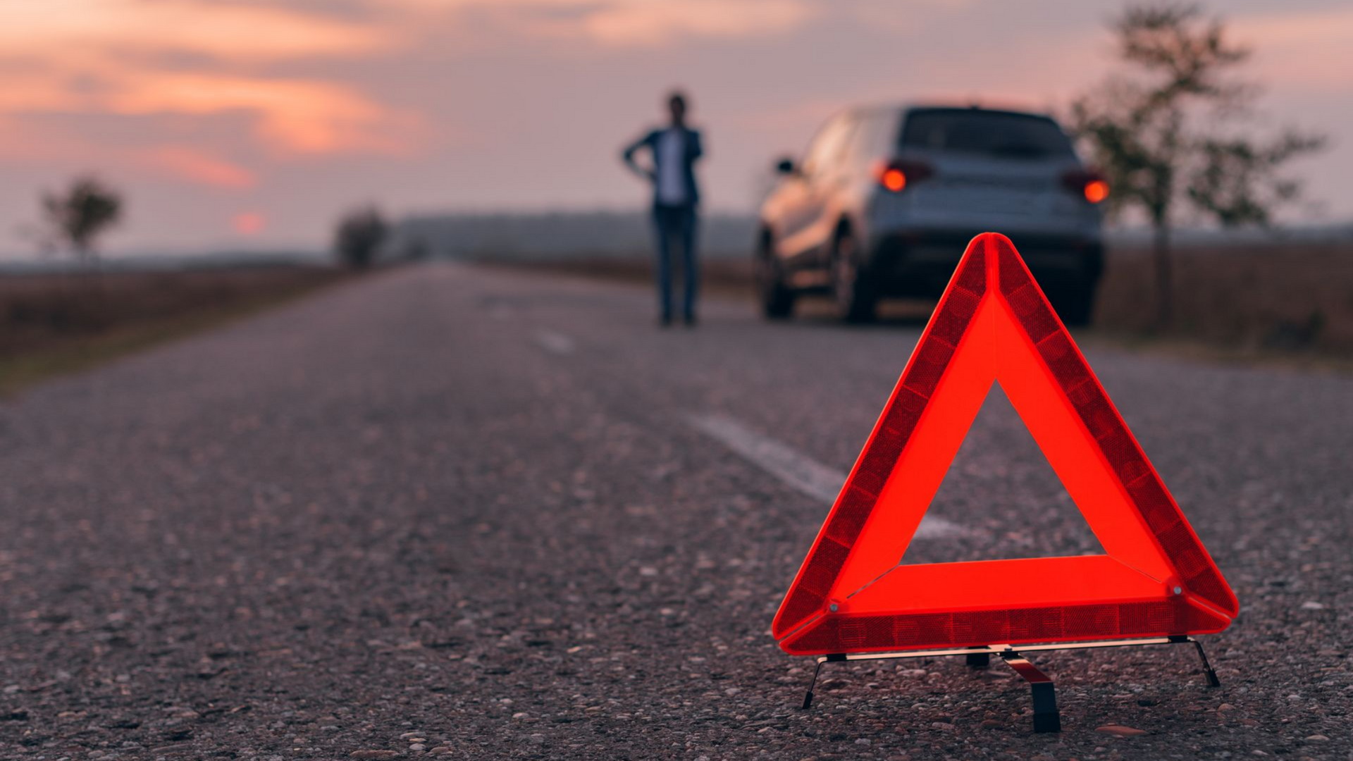 Une personne en panne sur une route avec un triangle en premier plan.