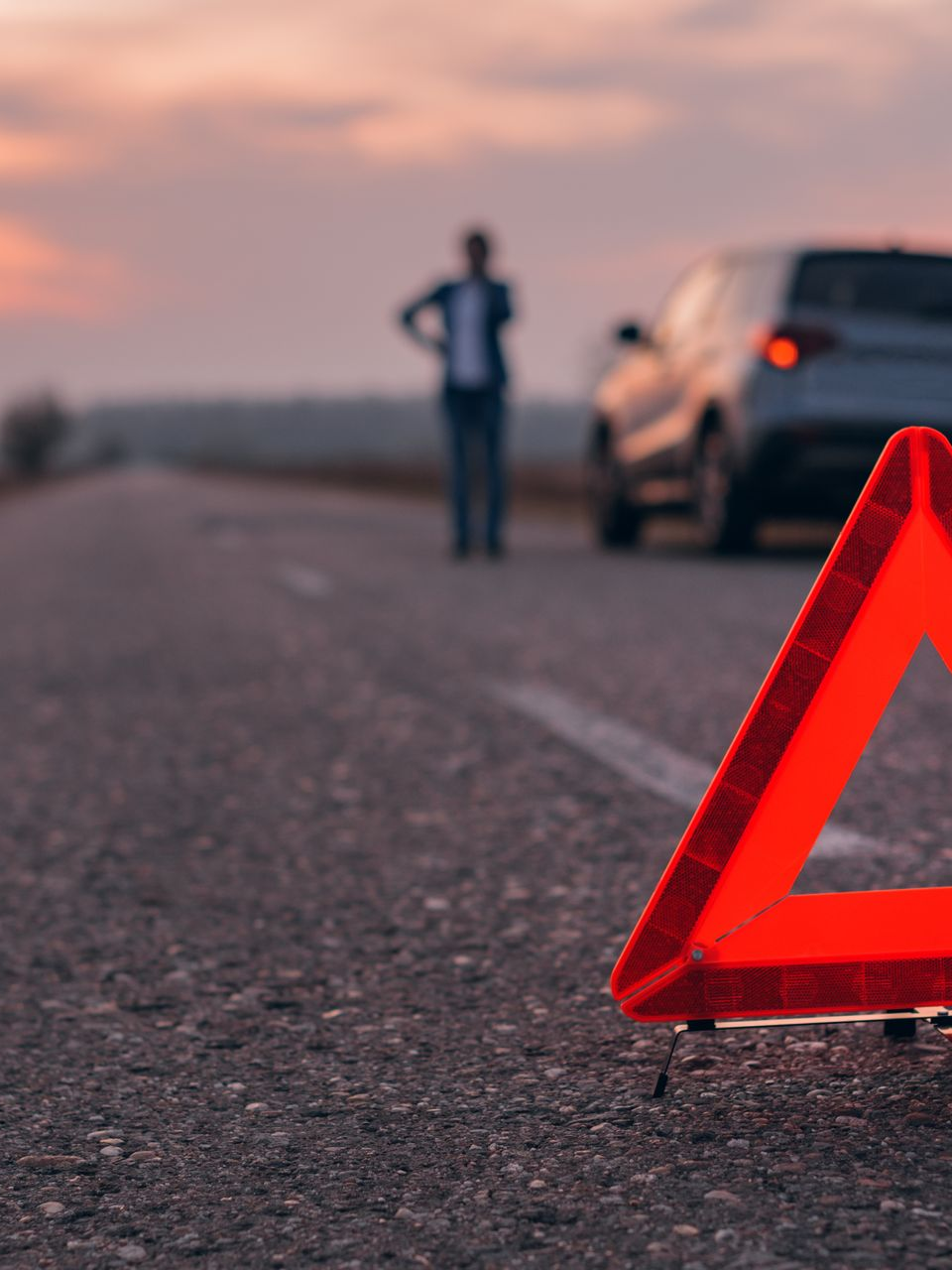 Une personne garée sur le bord d'une route avec un triangle en premier plan.