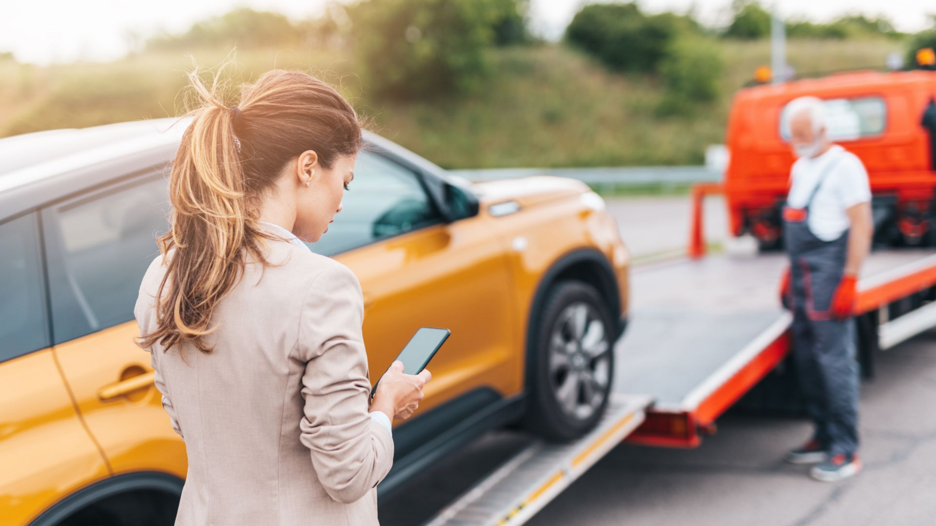 Un femme regarde son téléphone pendant qu'un dépanneur remorque sa voiture.