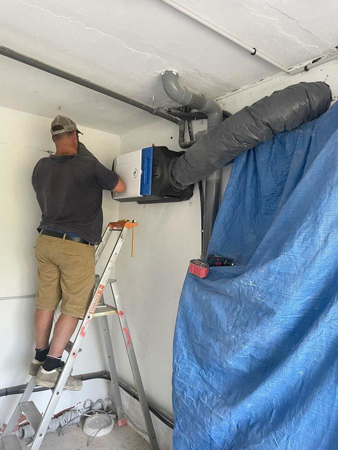 Installation d'une ventilation par un artisan sur un escabeau