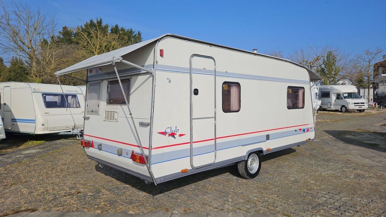 Une remorque blanche avec un auvent est garée sur un parking.