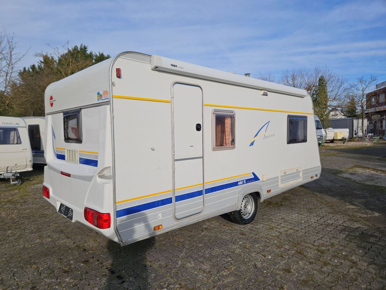 Une caravane blanche à rayures bleues et jaunes est garée à l'extérieur par une journée ensoleillée.