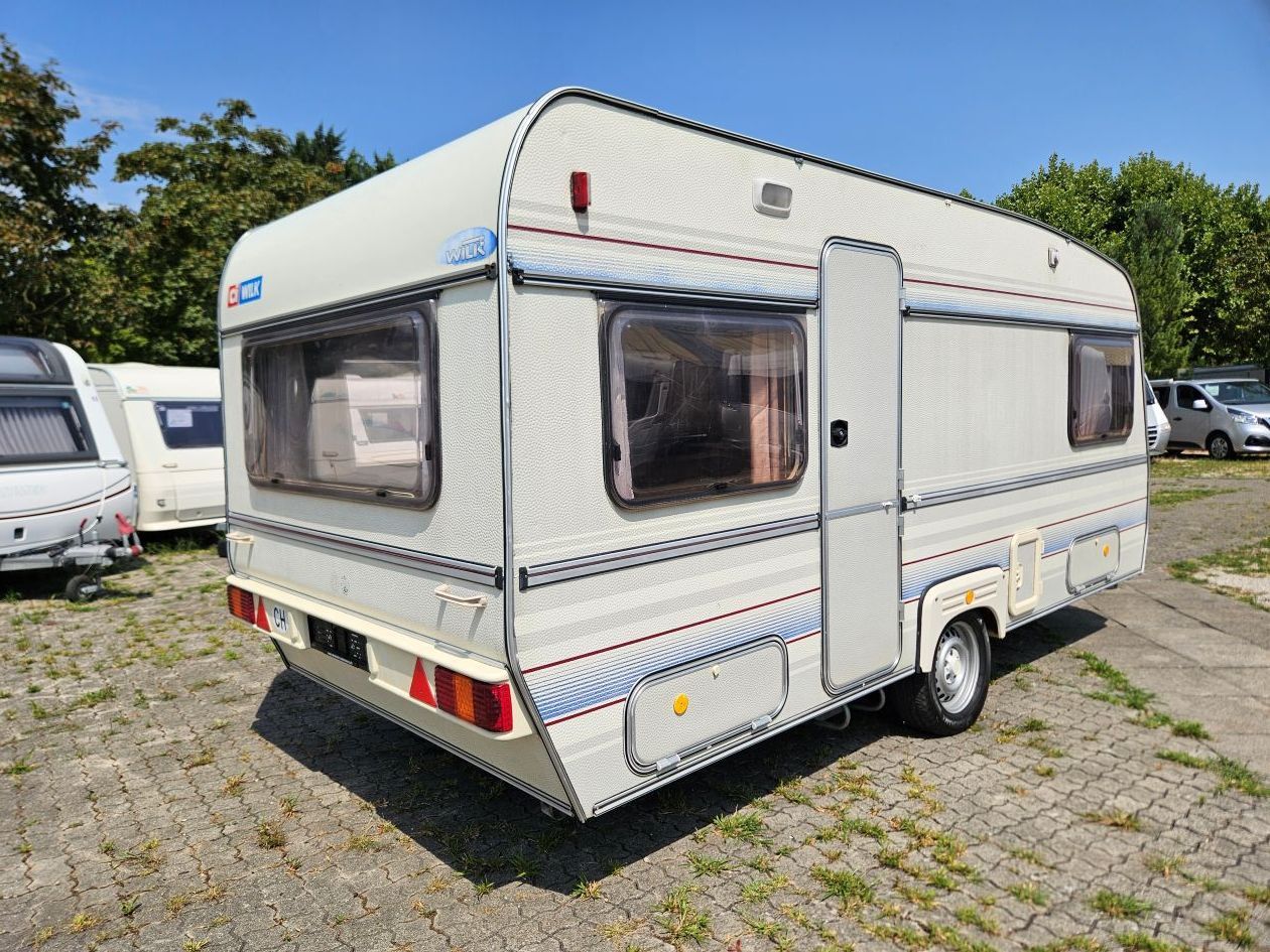 Caravane blanche avec fenêtres garée sur un terrain herbeux à l'extérieur