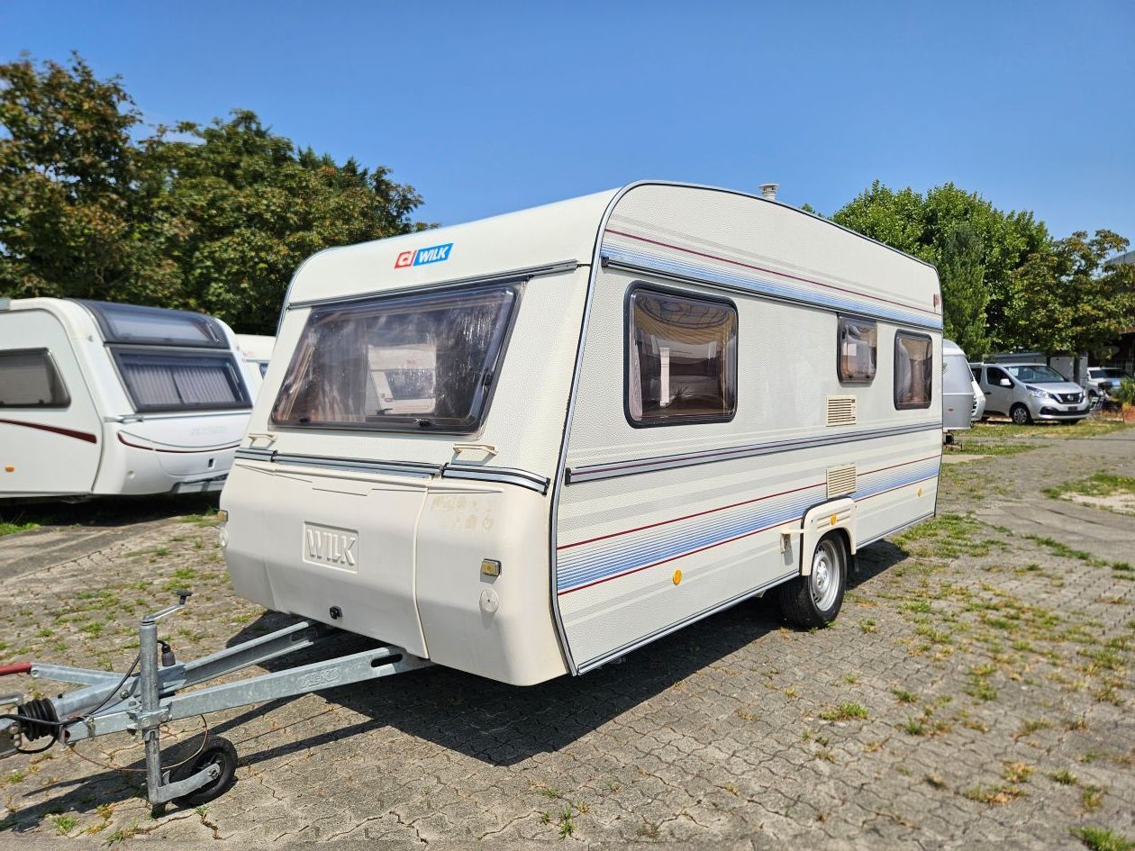 Petite caravane couleur blanche avec garée sur l'herbe, attelage de remorque visible.
