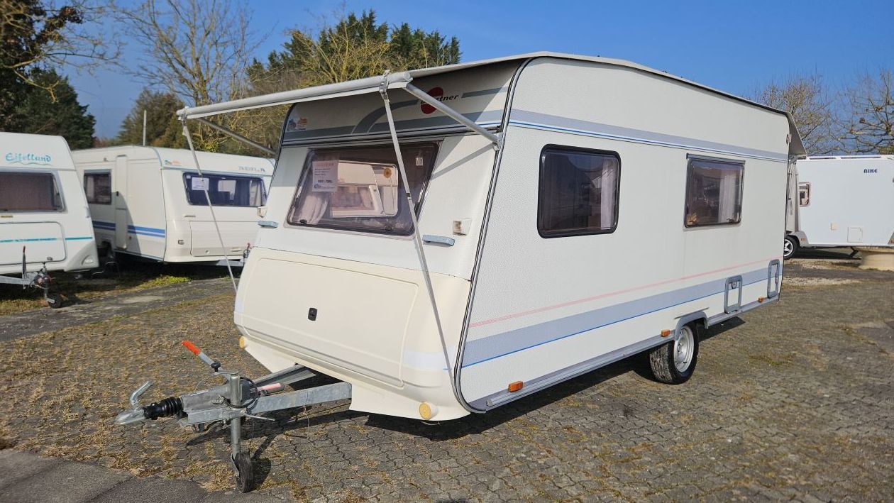 Une remorque blanche avec un auvent est garée sur un terrain en gravier.