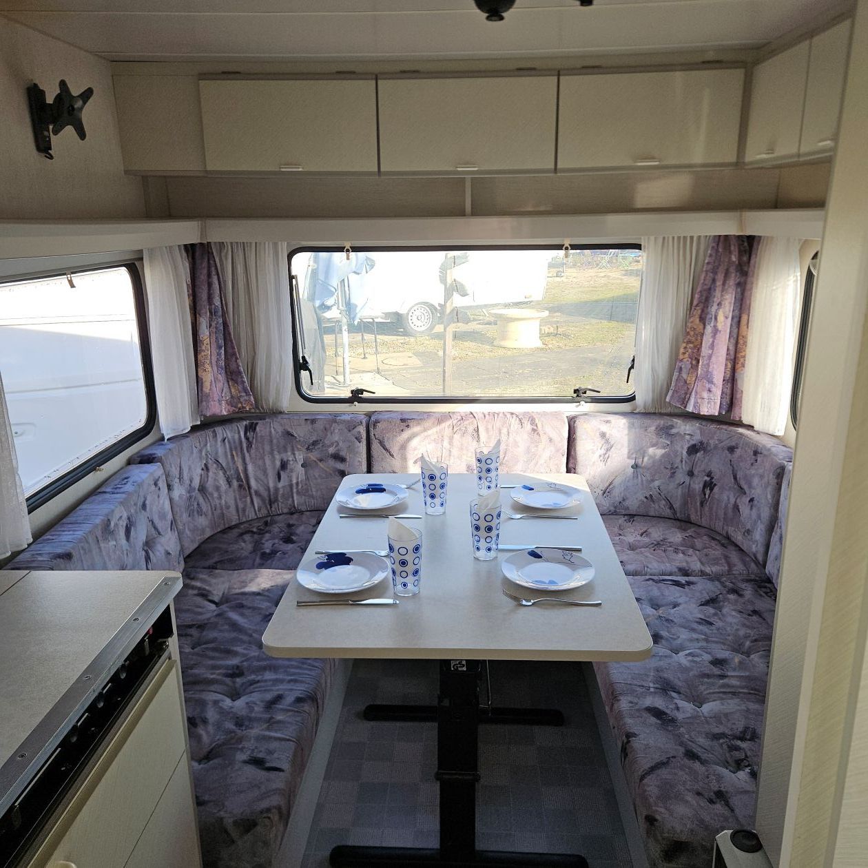 Intérieur d'un camping-car avec une table dressée pour un repas et des banquettes disposées en angle.