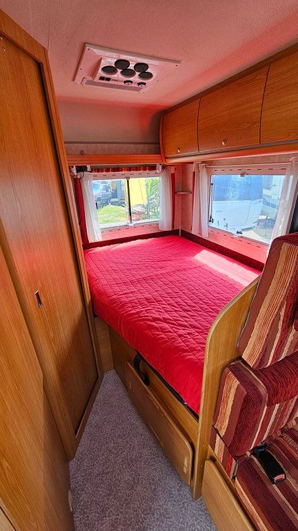 L'intérieur d'un camping-car avec un lit et un matelas rouge.
