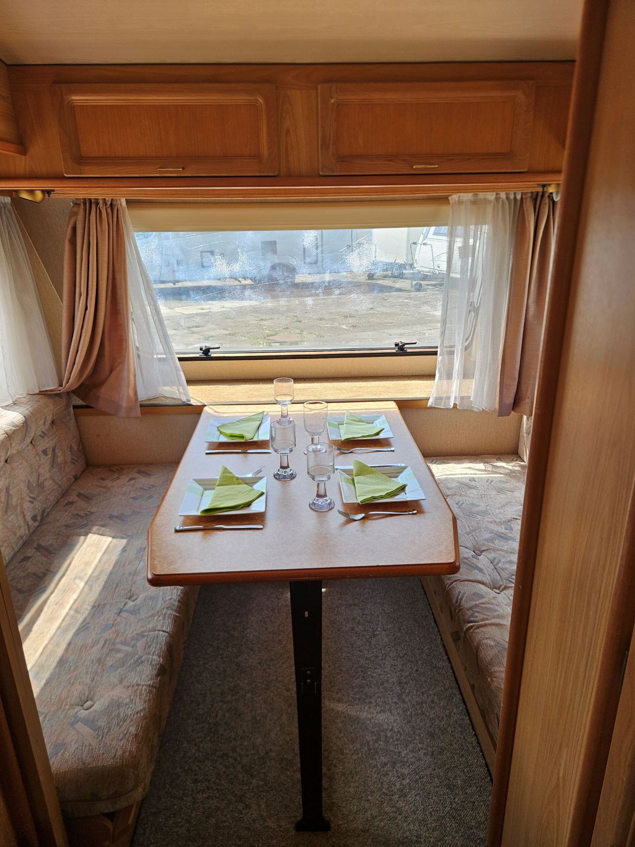 Petit coin repas dans un camping-car avec une table en bois, une banquette et une grande fenêtre offrant une belle vue.