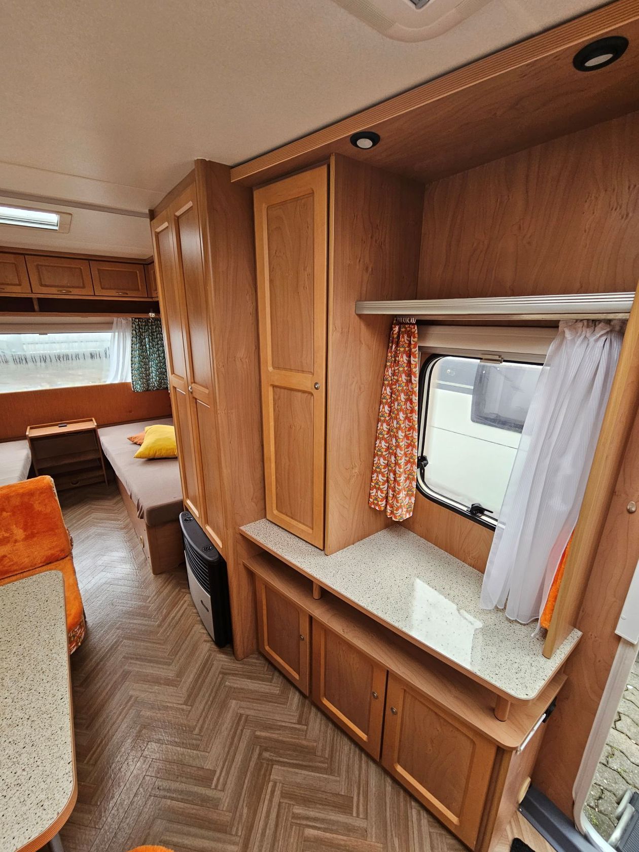 Intérieur d'une caravane en bois avec un coin salon, des placards, une fenêtre avec rideaux et un plan de travail.
