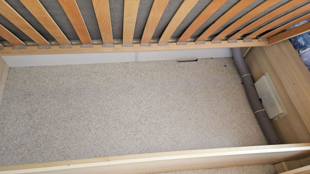 Un cadre de lit est posé sur un sol recouvert de moquette.