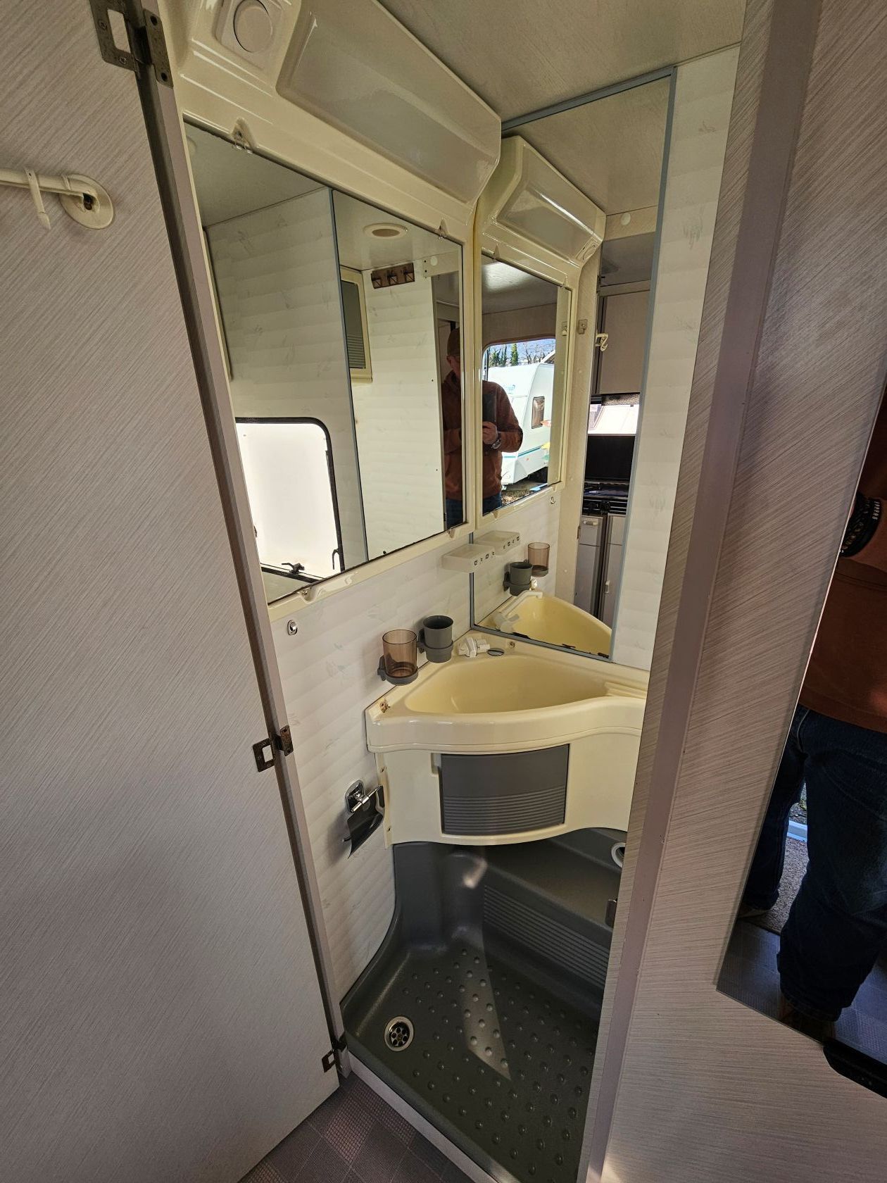 Intérieur de salle de bain de camping-car avec miroirs, lavabo et douche.