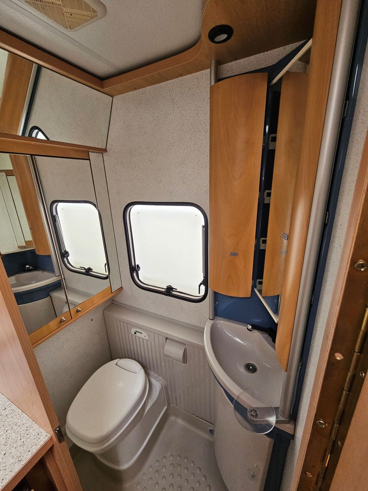 Petite salle de bain de camping-car avec toilettes, lavabo, miroir et fenêtre.