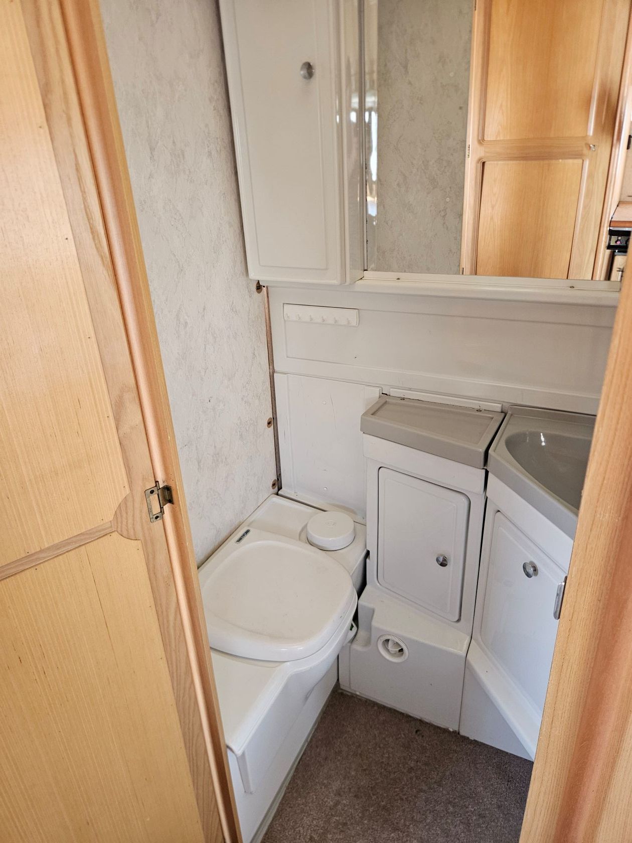 Salle de bain compacte pour camping-car avec toilettes, lavabo et armoire à miroir beige et blanche.