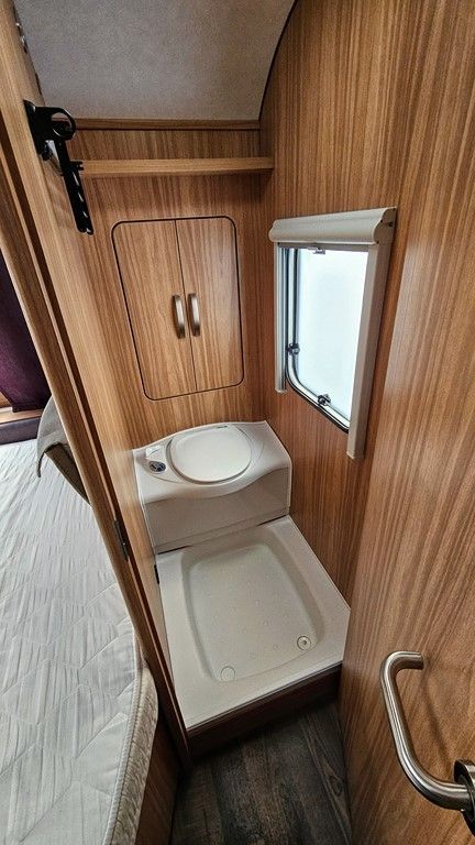 Une salle de bain dans un camping-car avec toilettes, lavabo et fenêtre.
