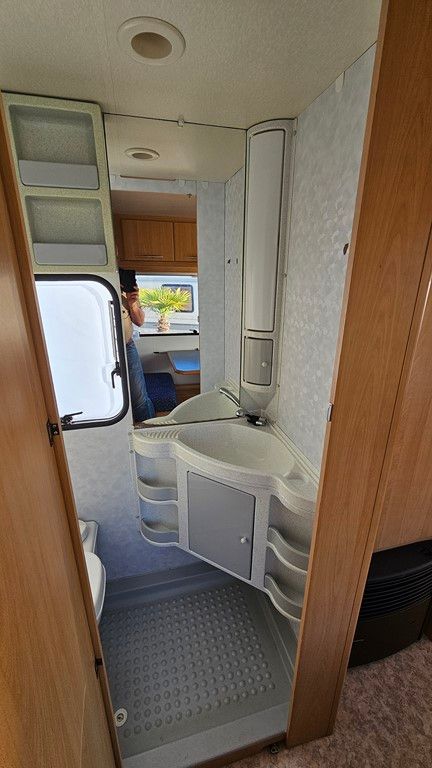 Une salle de bain dans un camping-car avec un lavabo, des toilettes et un miroir.