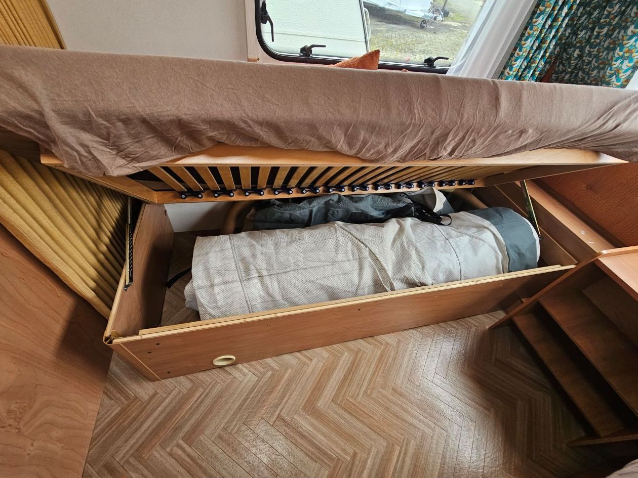 Tiroir en bois sous un lit dans un camping-car, contenant la literie.