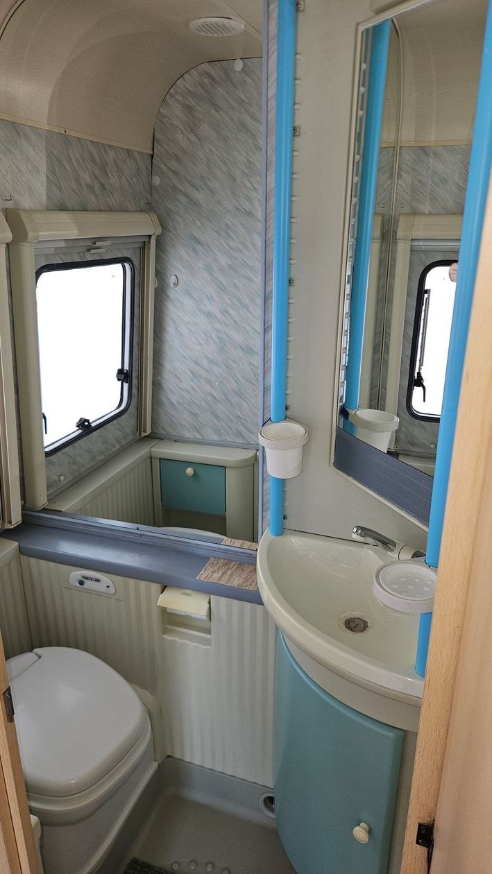 Une salle de bain dans un camping-car avec WC, lavabo et miroir.