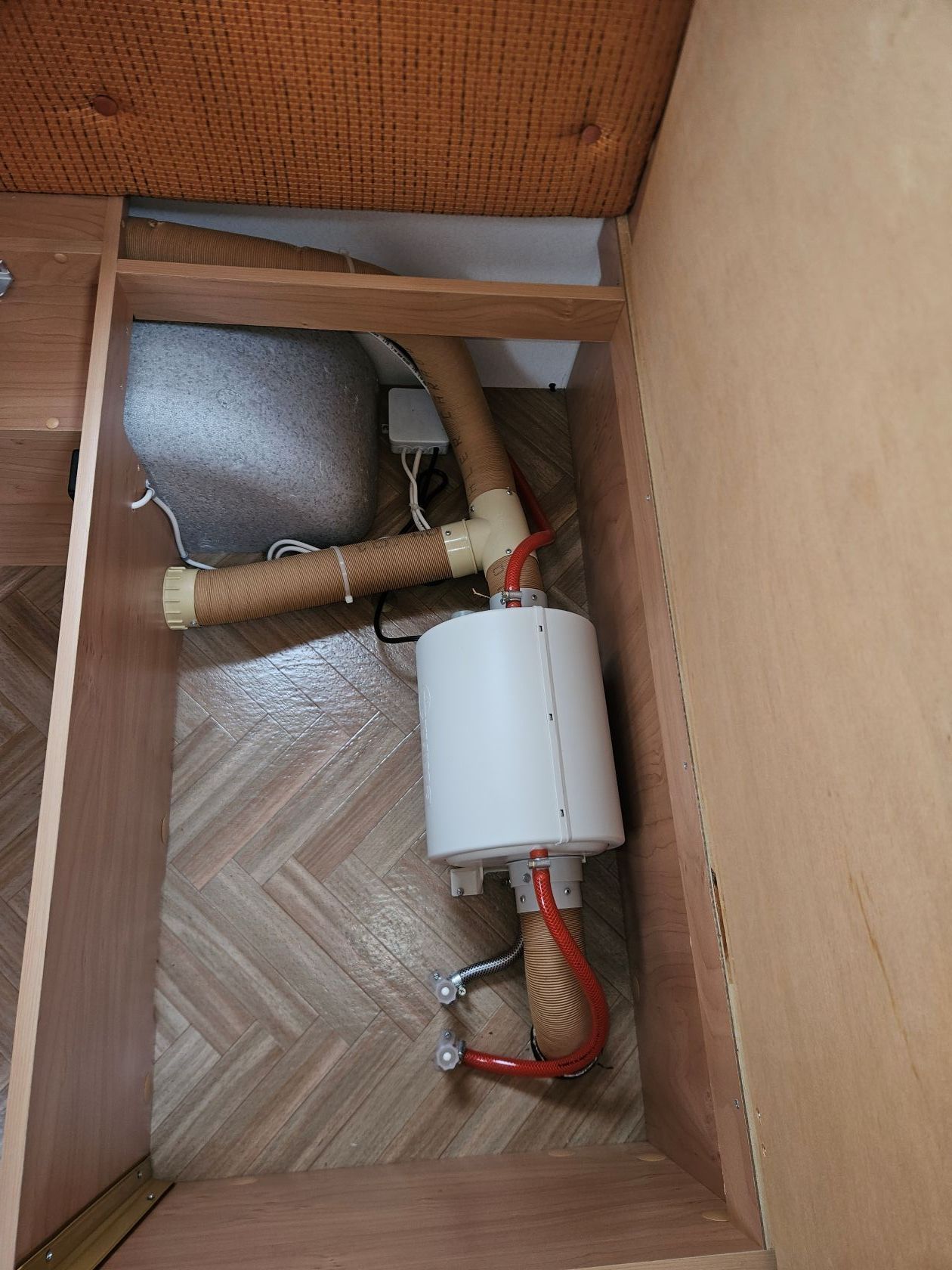 Chauffe-eau blanc dans un meuble en bois, avec tuyaux et câblage raccordés.