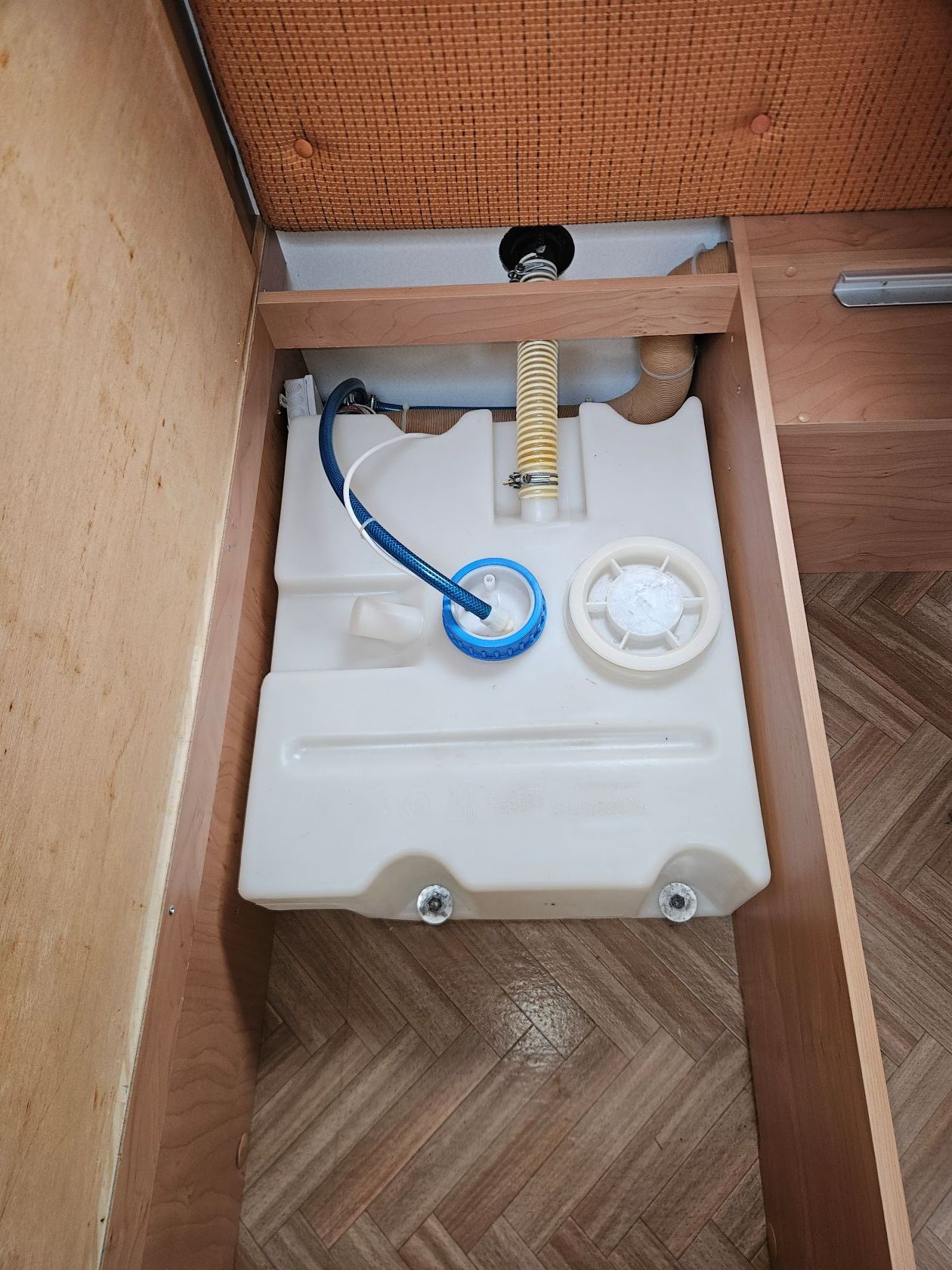 Un réservoir d'eau rectangulaire dans un compartiment en bois, avec des éléments bleus et blancs.