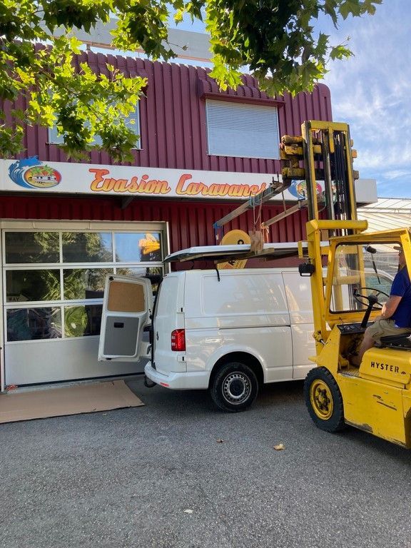 Une camionnette blanche est garée devant un bâtiment sur lequel est écrit 