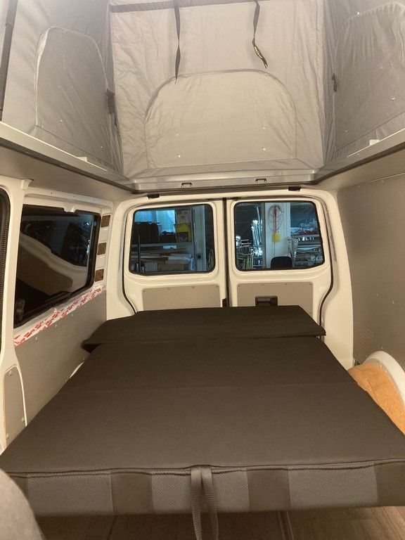 L'intérieur d'une camionnette avec un lit et une tente sur le dessus.