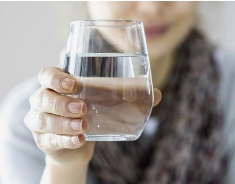 Mano sosteniendo un vaso de agua transparente frente a un fondo borroso.