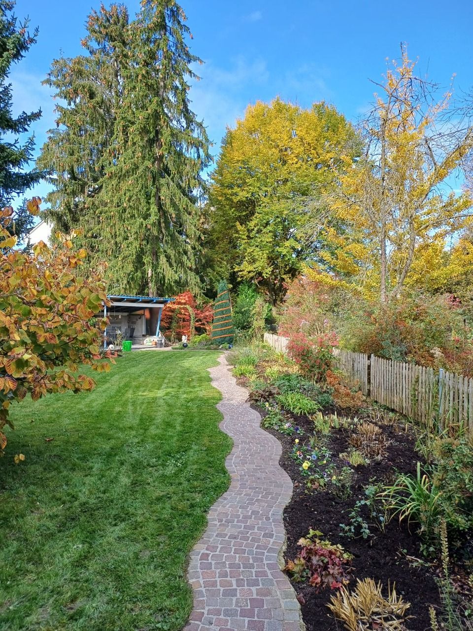Ein Ziegelweg führt zu einem Haus in einem von Bäumen umgebenen Garten. Foto von der Viridis Gärten GmbH