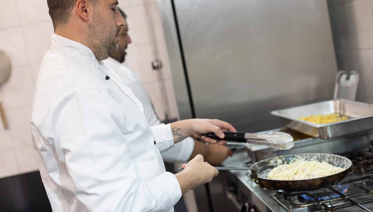 Ein Mann in einem gelben Hemd bereitet Essen auf einem Grill in einer Küche .