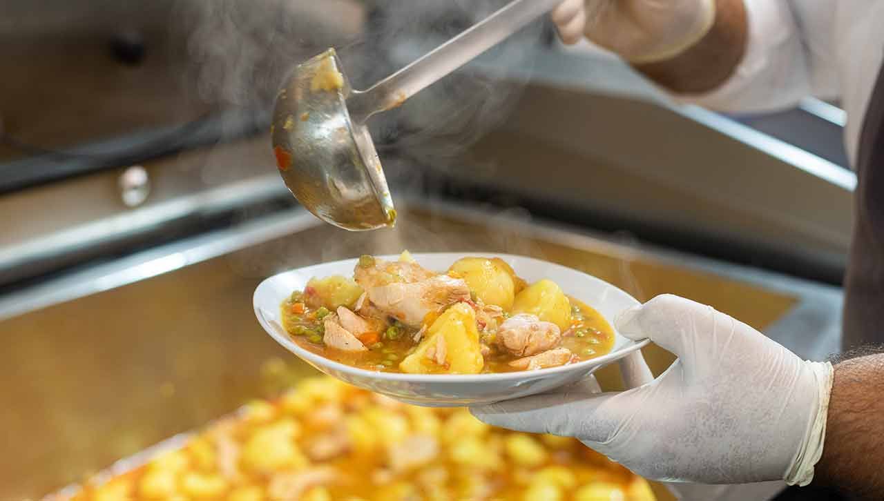 Ein Koch gießt Suppe aus einer Gabel in einen Teller .