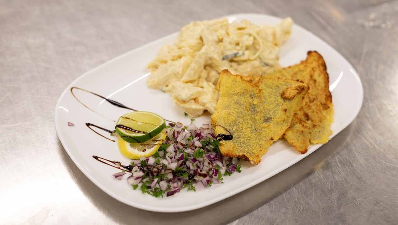 ein weißer Teller mit einem Stück Fisch und einem Salat auf einem Tisch .