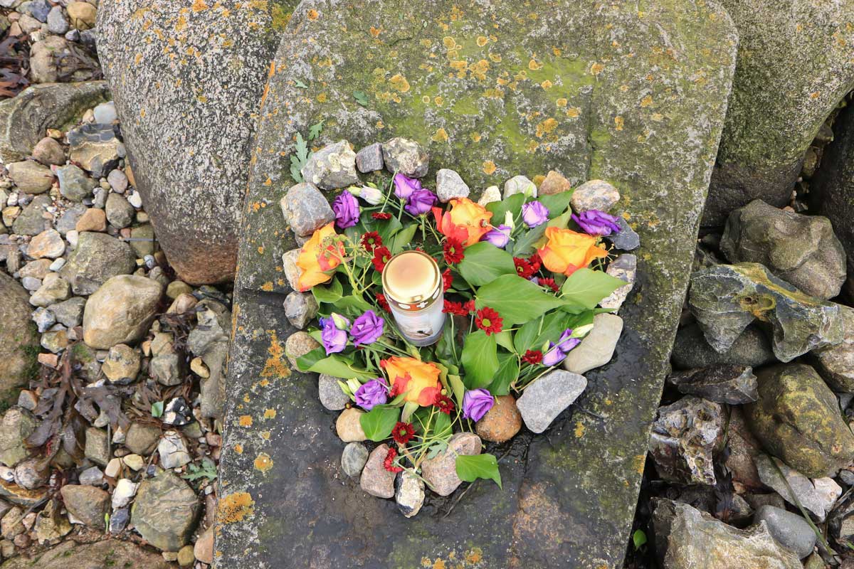 Cœur fait en cailloux et rempli de fleurs avec une bougie au centre