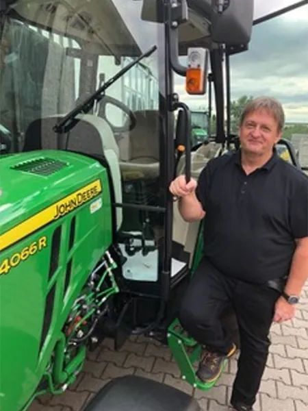 Ein Mann steht neben einem grünen John Deere Traktor