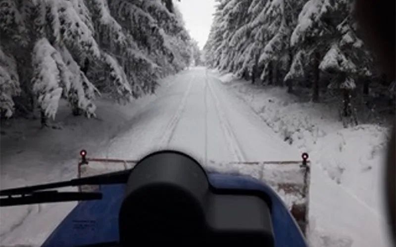 Ein Schneepflug fährt eine verschneite Straße im Wald entlang.