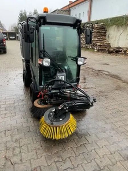 Eine Straßenkehrmaschine fährt eine Ziegelsteinstraße entlang.