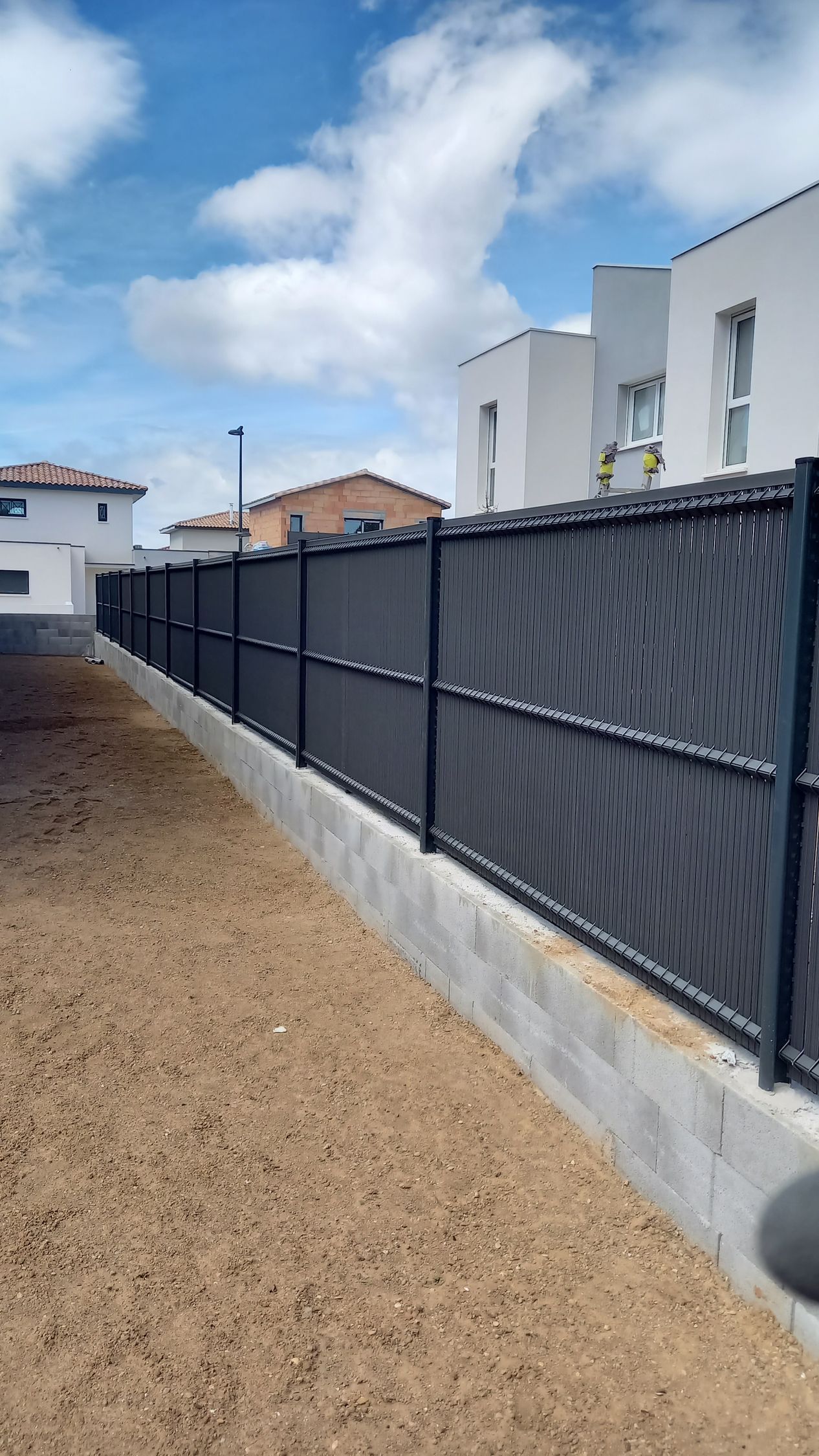 Palissades noires sur un muret en parpaing