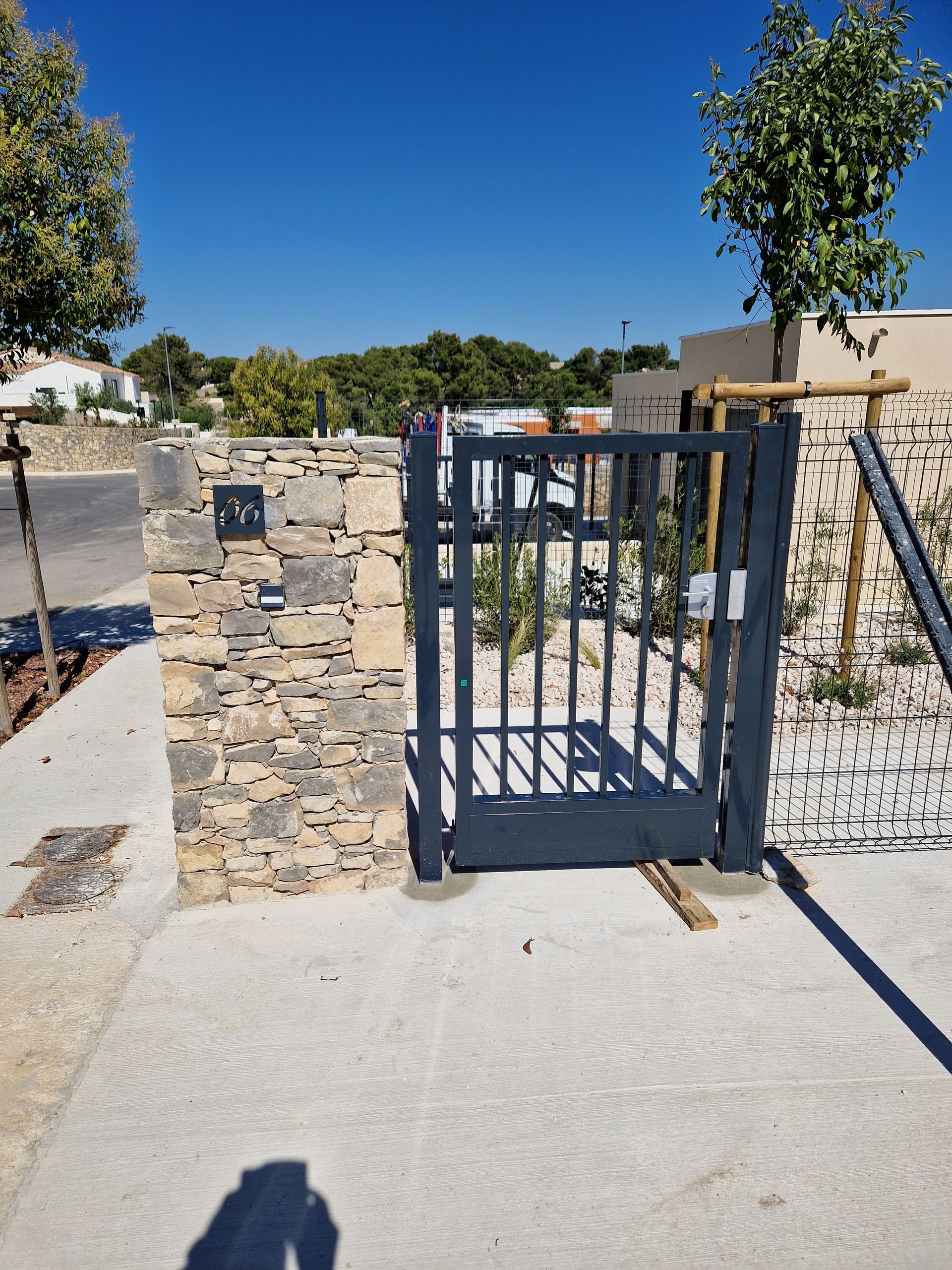 Vue frontale d'un portail électrique avec mur de pierre et grillage